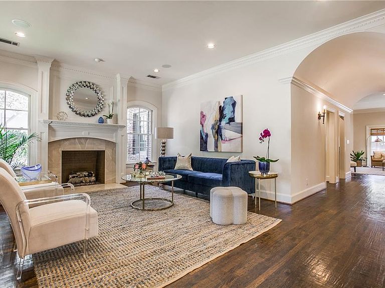 Great room at 4501 Livingston, with a second stone fireplace and round sunburst mirror over the mantel, a deep navy velvet sofa on a natural fiber rug, and an arched corridor opening to the rest of the home