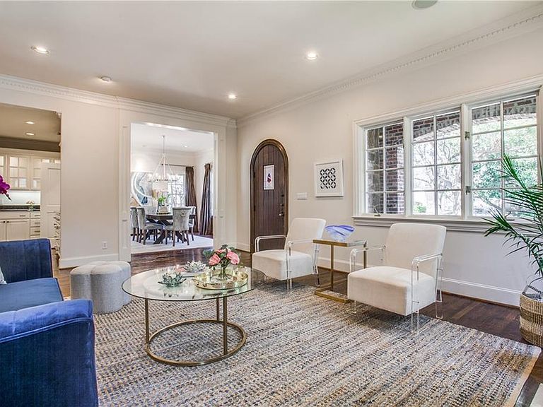 Living area looking back toward the dining room at 4501 Livingston, with leaded windows admitting daylight, the arched wood door visible in the background, and acrylic-and-brass chairs framing a glass coffee table