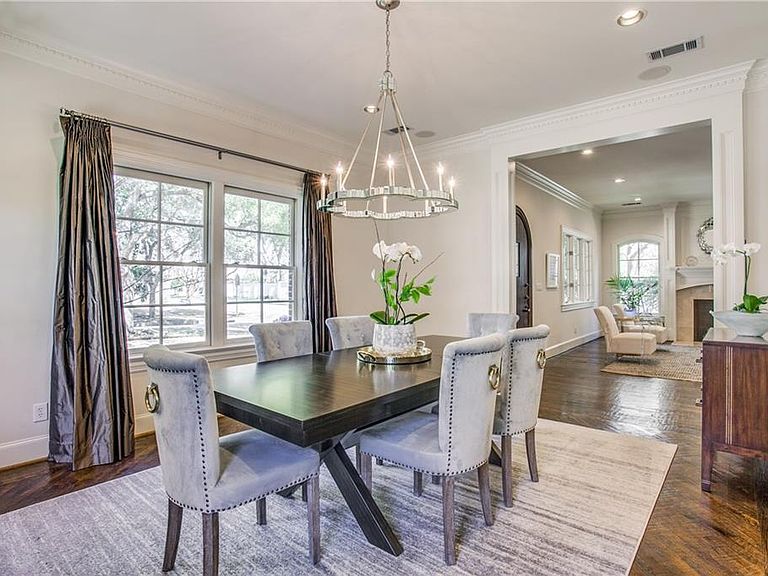 Formal dining room at 4501 Livingston, with a long dark wood table, six tufted upholstered chairs, a tiered chandelier, deep silk curtains framing leaded windows, and an orchid centerpiece on a silver tray
